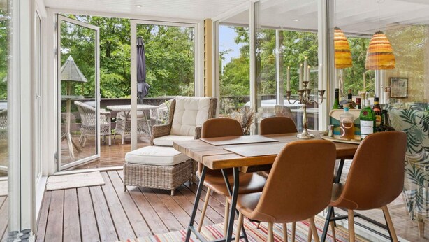 A modern outdoor dining area with a glass enclosure, wicker furniture, and a view of the greenery outside. - 4 Star Holiday Home in Hemmet (Hemmet)
