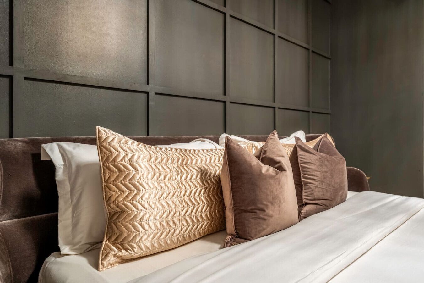 A bed with a dark headboard and multiple pillows in various patterns and textures.