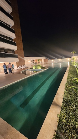 A nighttime view of a swimming pool with a modern building in the background.