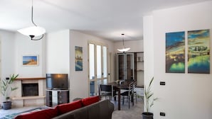 Un salon avec une cheminée, un téléviseur, un coin repas avec des chaises et des œuvres d’art accrochées aux murs.