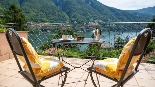 Une terrasse avec deux chaises, une table et une vue sur un lac et des montagnes.