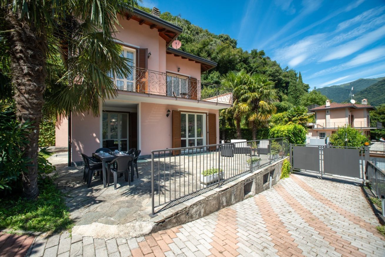A two-story house with a patio, outdoor furniture, and a view of the surrounding hills.