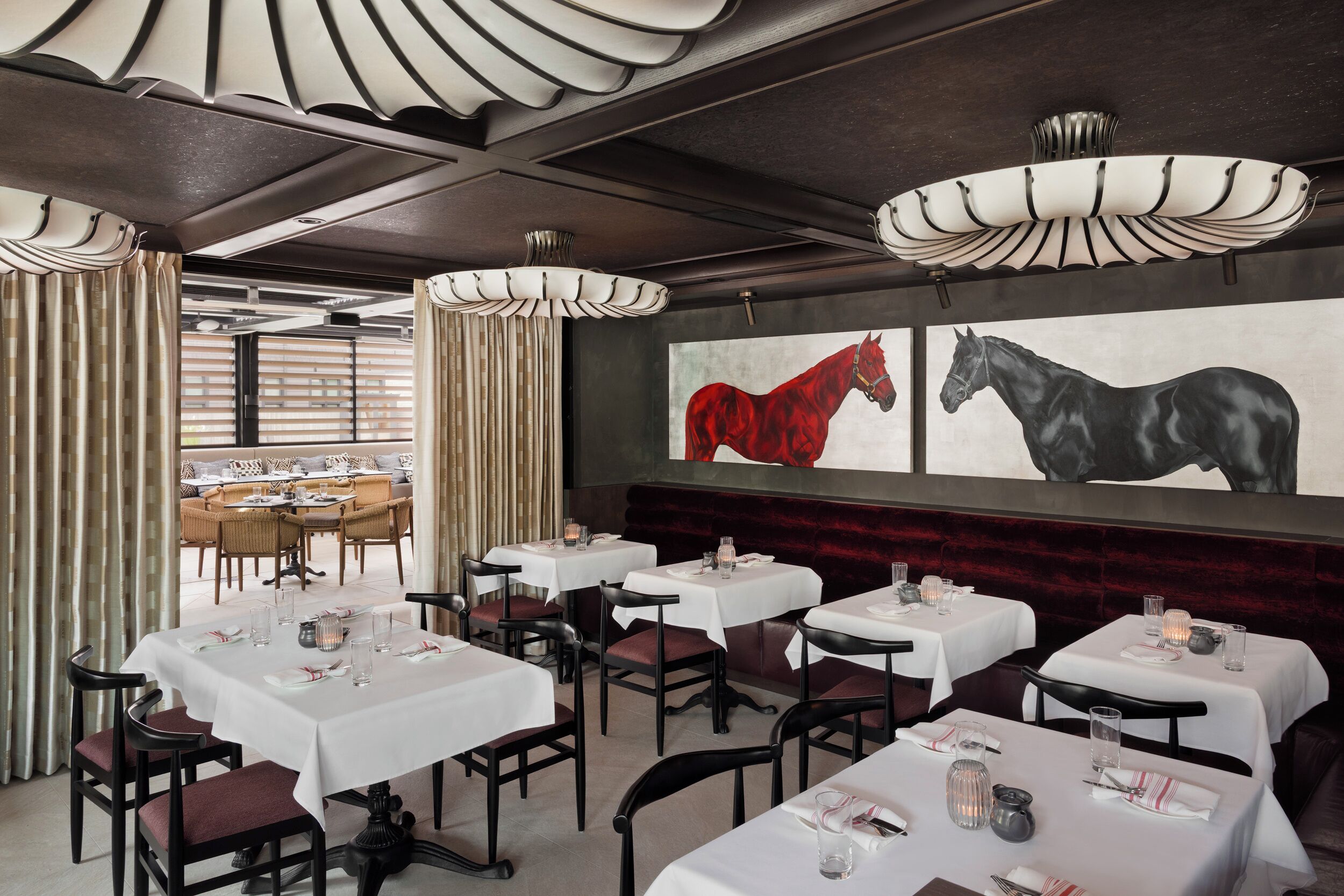 Un restaurante con mesas dispuestas para comer, un cuadro grande de un caballo en la pared y vistas del área de terraza.