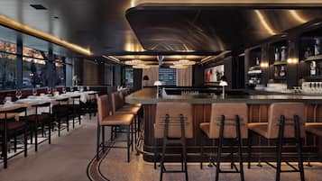 A modern bar area with a curved counter, bar stools, and a view of the outside.