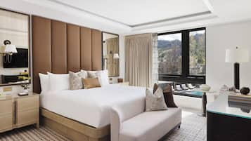 Een moderne hotelkamer met een groot bed, een bank, een bureau en uitzicht op een bergachtig landschap.