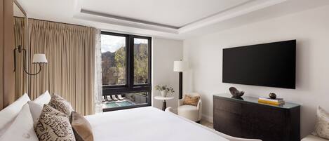Habitación de hotel con una cama grande, televisor, escritorio y vistas a la montaña.