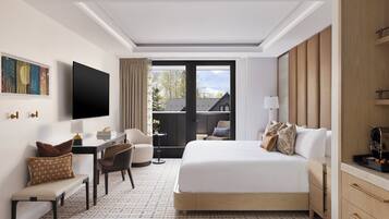 Habitación de hotel con cama, escritorio, silla, televisión y vistas al exterior.