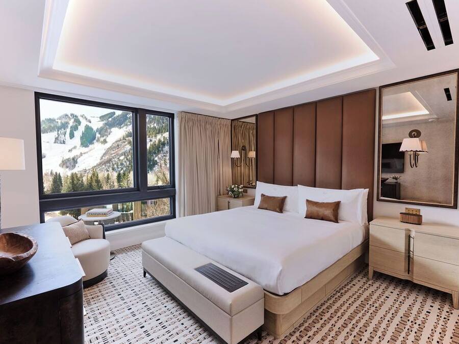 Habitació d'hotel moderna amb un llit gran, zona de seients amb vista a les muntanyes, taula auxiliar de fusta i un mirall gran.