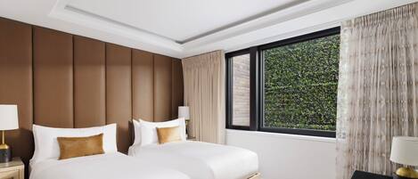 Hotelkamer met twee bedden, een bureau, een stoel, een raam met gordijnen en uitzicht op groen.