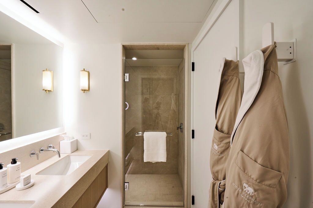A modern bathroom with a large mirror, two wall-mounted lights, a shower area, and a towel rack.