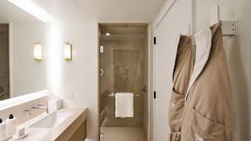 A modern bathroom with a large mirror, two wall-mounted lights, a shower area, and a towel rack.