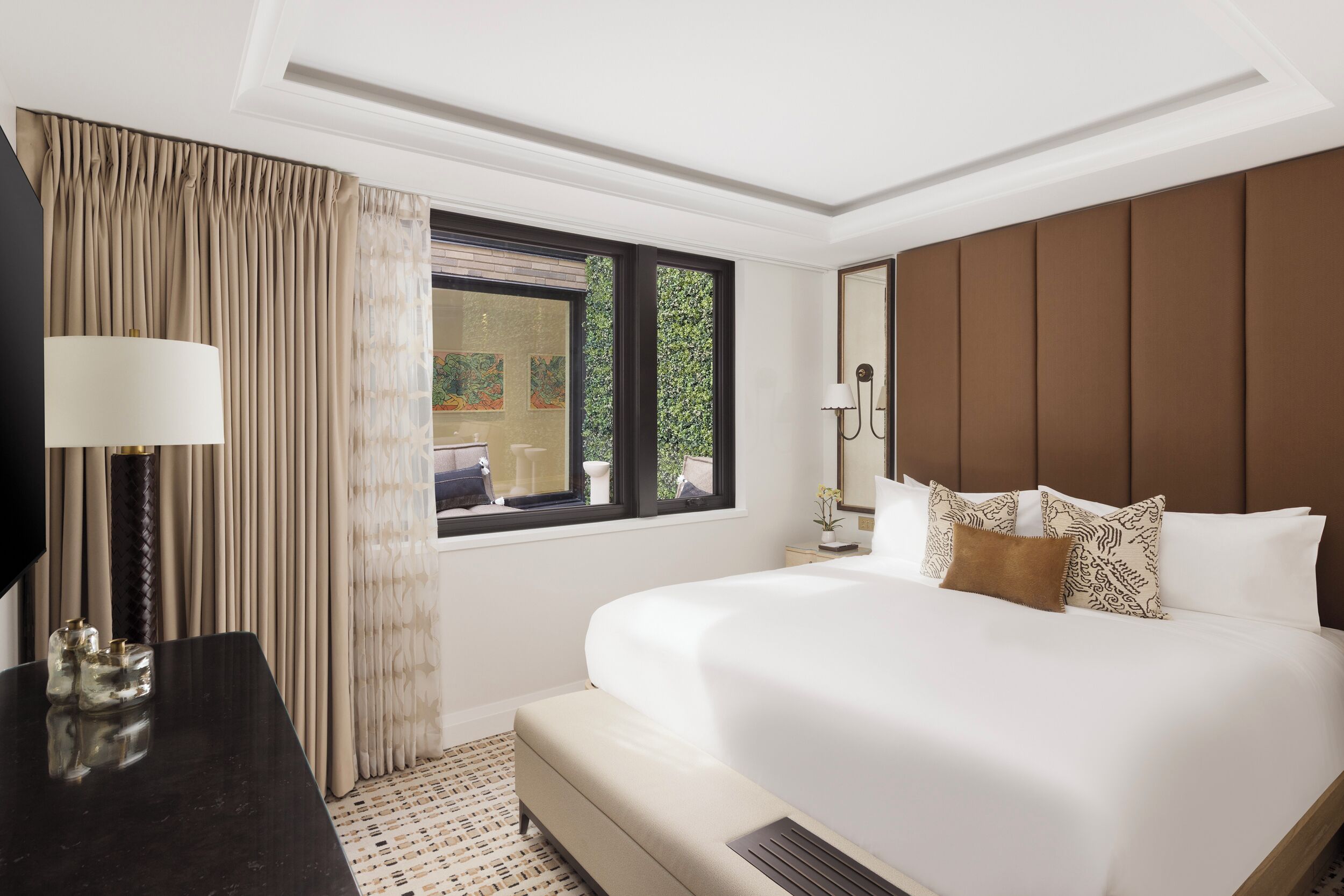 A hotel room with a large bed, a desk, a TV, and a window with curtains.