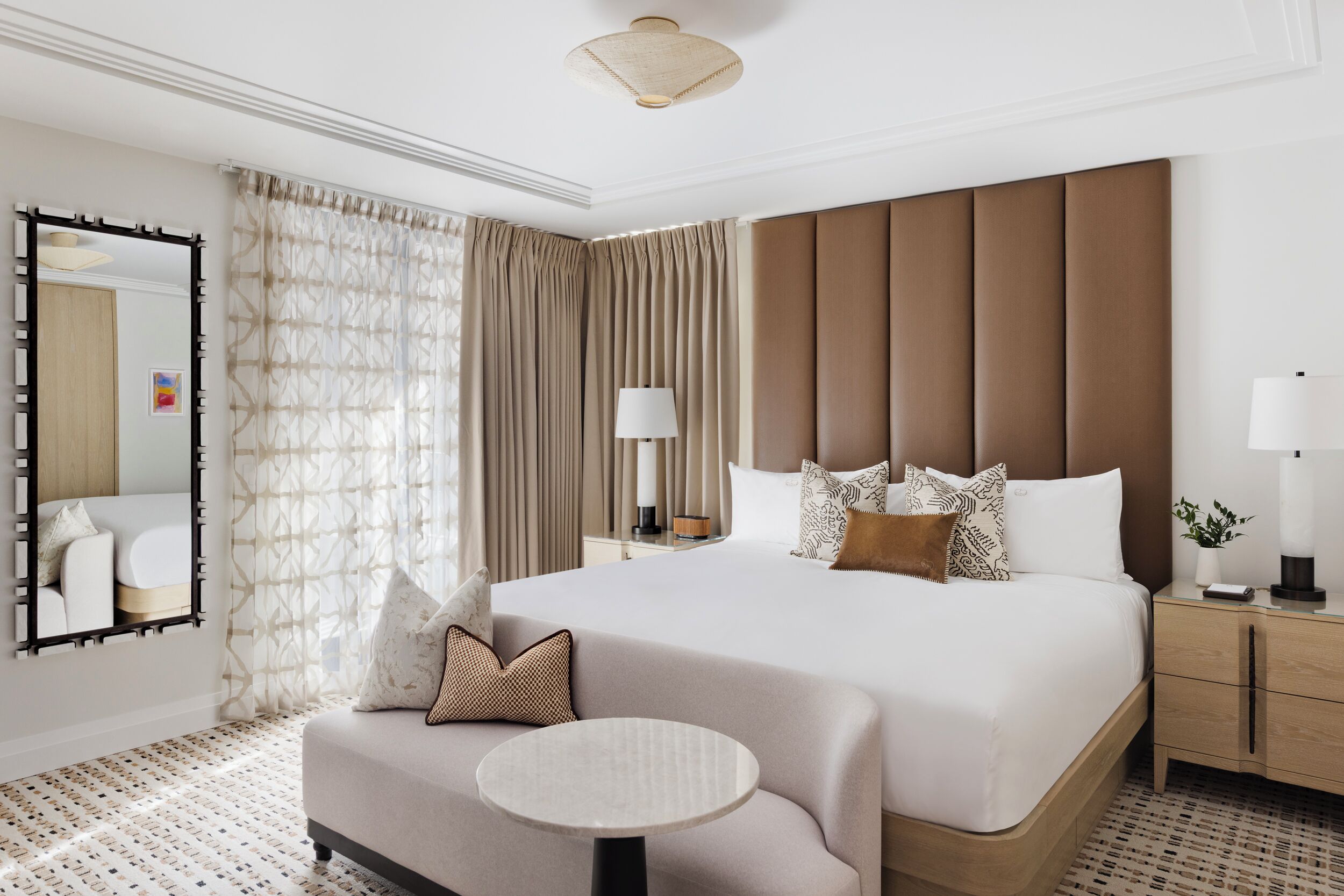 A hotel room with a large bed, bedside tables, a round table, a mirror, and curtains.