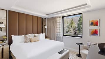 A hotel room with a large bed, a desk, a chair, a window with a view, and artwork on the wall.