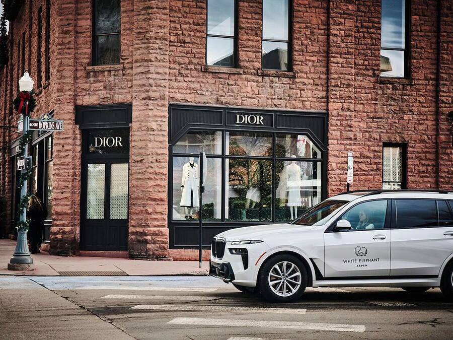 Un SUV blanco estacionado frente a un edificio de ladrillo con una tienda de Dior.