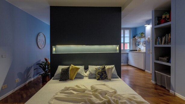 Une chambre à coucher avec un lit, une table de chevet et une commode. Il y a une fenêtre avec des rideaux, une horloge murale et une bibliothèque.