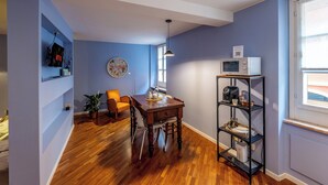 Un coin repas comprenant une table en bois, des chaises et une étagère en métal noir où sont rangés des appareils de cuisine.