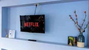 Un téléviseur fixé au mur, affichant le logo de Netflix, une télécommande, un certificat encadré, un livre et un vase avec des branches.