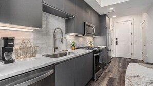 A modern kitchen with grey cabinetry, a stainless steel sink, a built-in microwave, and a gas stove. - A Cozy Luxurious Stay Buckhead Atlanta (Atlanta)