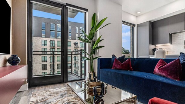 A modern living room with a glass coffee table, a blue sofa, and a large window overlooking a building. - A Cozy Luxurious Stay Buckhead Atlanta (Atlanta)