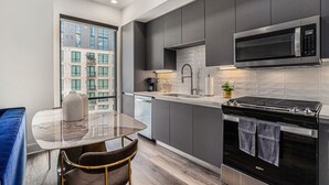 A modern kitchen with grey cabinets, a black microwave, a stove, and a dining area with a marble table and a chair. - A Cozy Luxurious Stay Buckhead Atlanta (Atlanta)