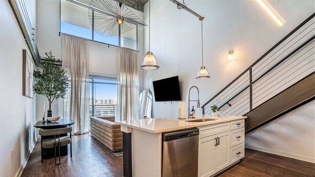 A modern kitchen with a dishwasher, a dining area with a table and chairs, and a staircase leading to an upper level. - Modern LuxuryLoft In The Heart Of Atlantic Station (Atlanta)