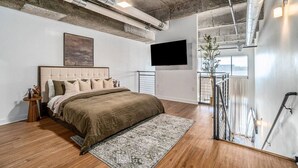 A modern bedroom with a large bed, a mounted TV, and a view of the city through a window. - Modern LuxuryLoft In The Heart Of Atlantic Station (Atlanta)