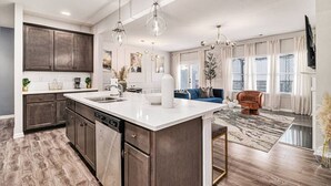 A modern kitchen with a large island, dark wood cabinets, and pendant lighting.