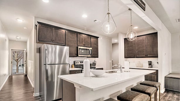 A modern kitchen with a large island, stainless steel appliances, and dark wood cabinets.