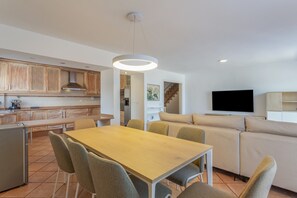 A modern kitchen with wooden cabinets, a dining table with chairs, a sofa, and a flat-screen TV.