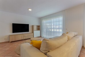 A living room with a flat-screen TV, a beige sofa, a small round table, and a cabinet.