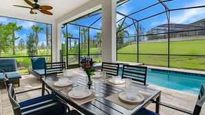 A poolside dining area with a table set for four, outdoor seating, and a view of a swimming pool and greenery.