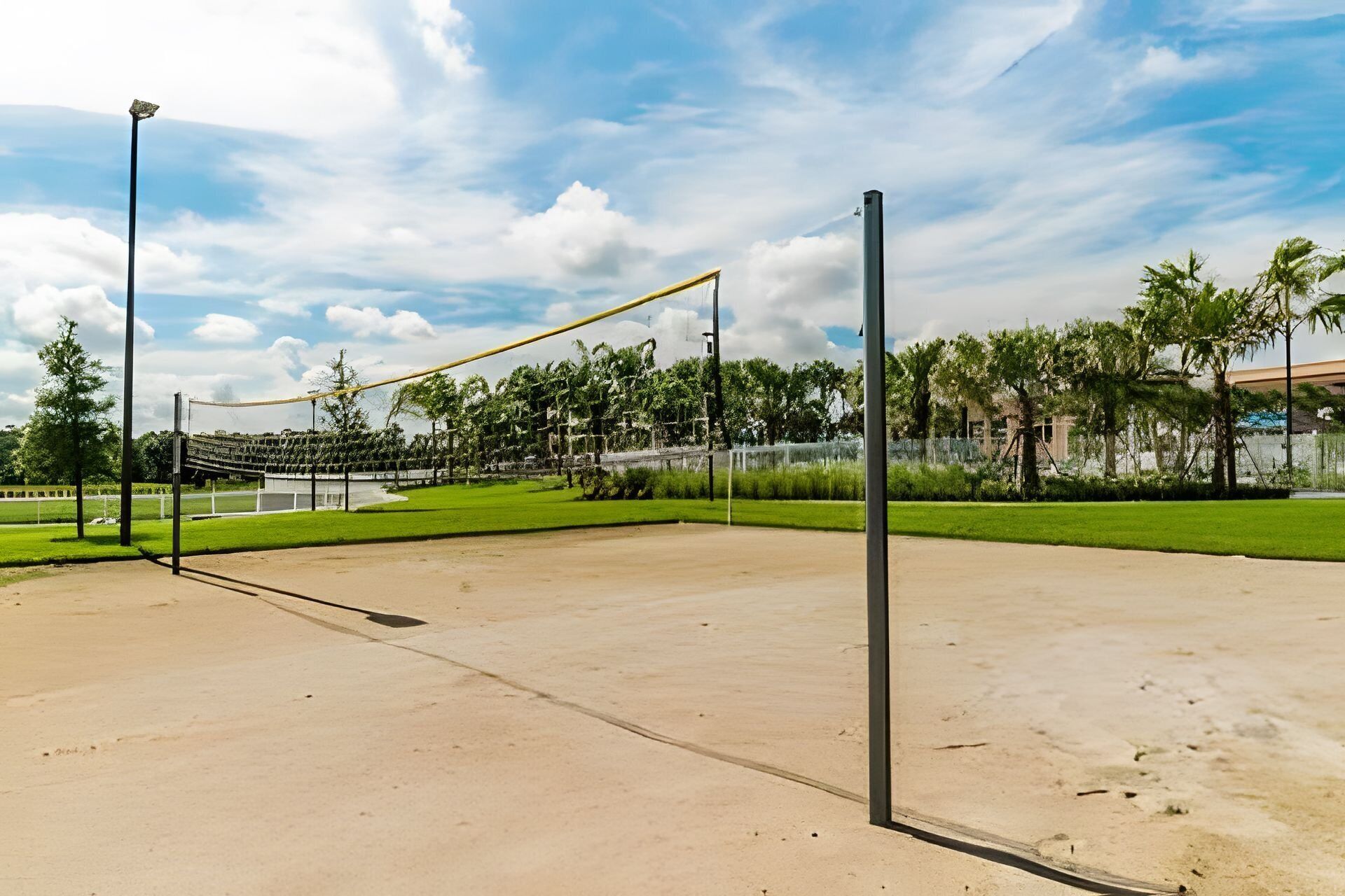 An outdoor volleyball court with a net, surrounded by greenery and a clear sky.