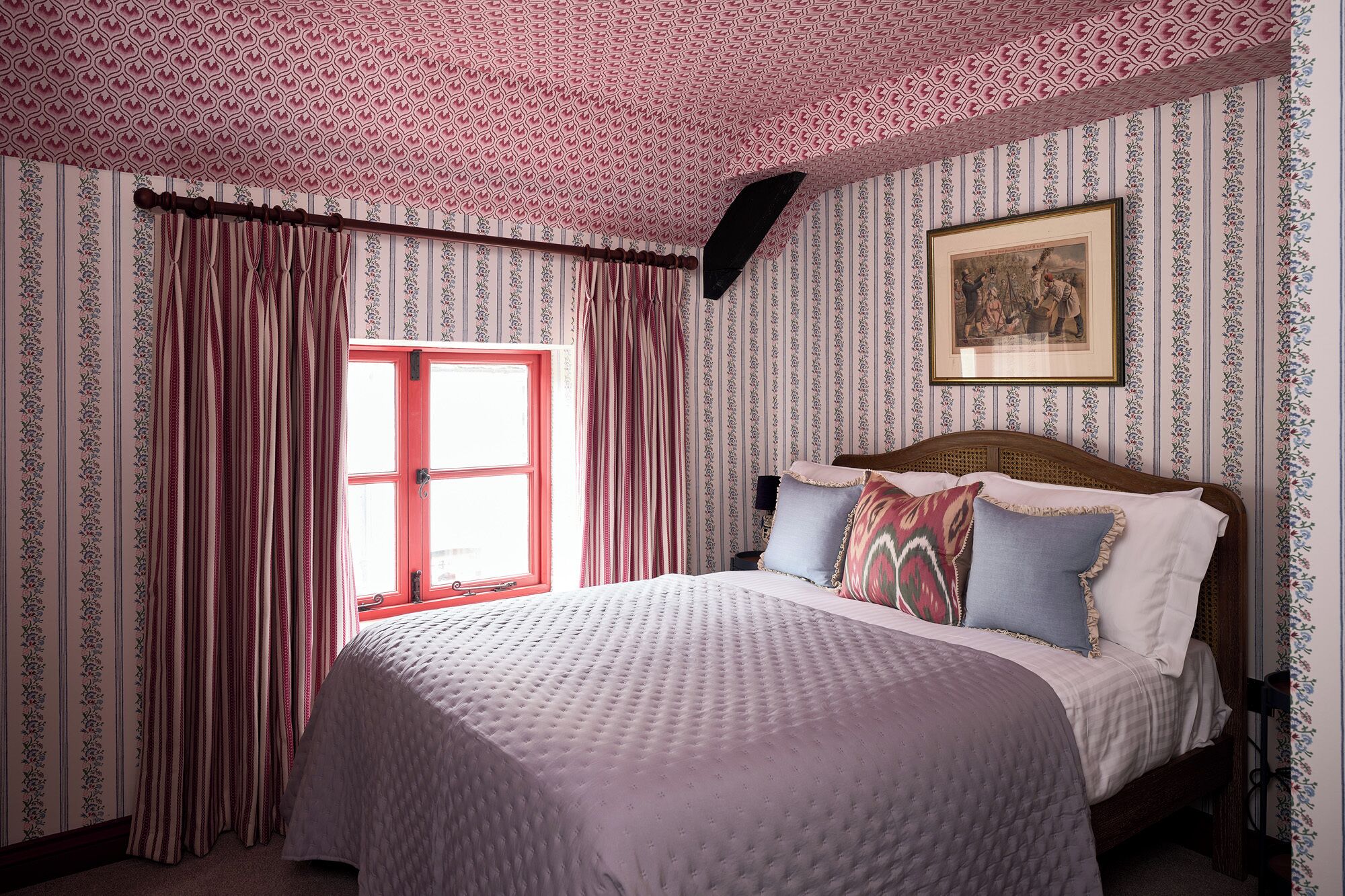 Een slaapkamer met een bed, gordijnen, een raam en een lijst met een afbeelding aan de muur.