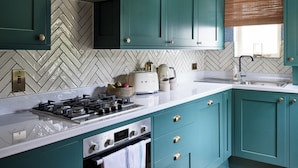 A kitchen with teal cabinets, a gas stove, a Bosch range hood, and a herringbone-patterned backsplash.