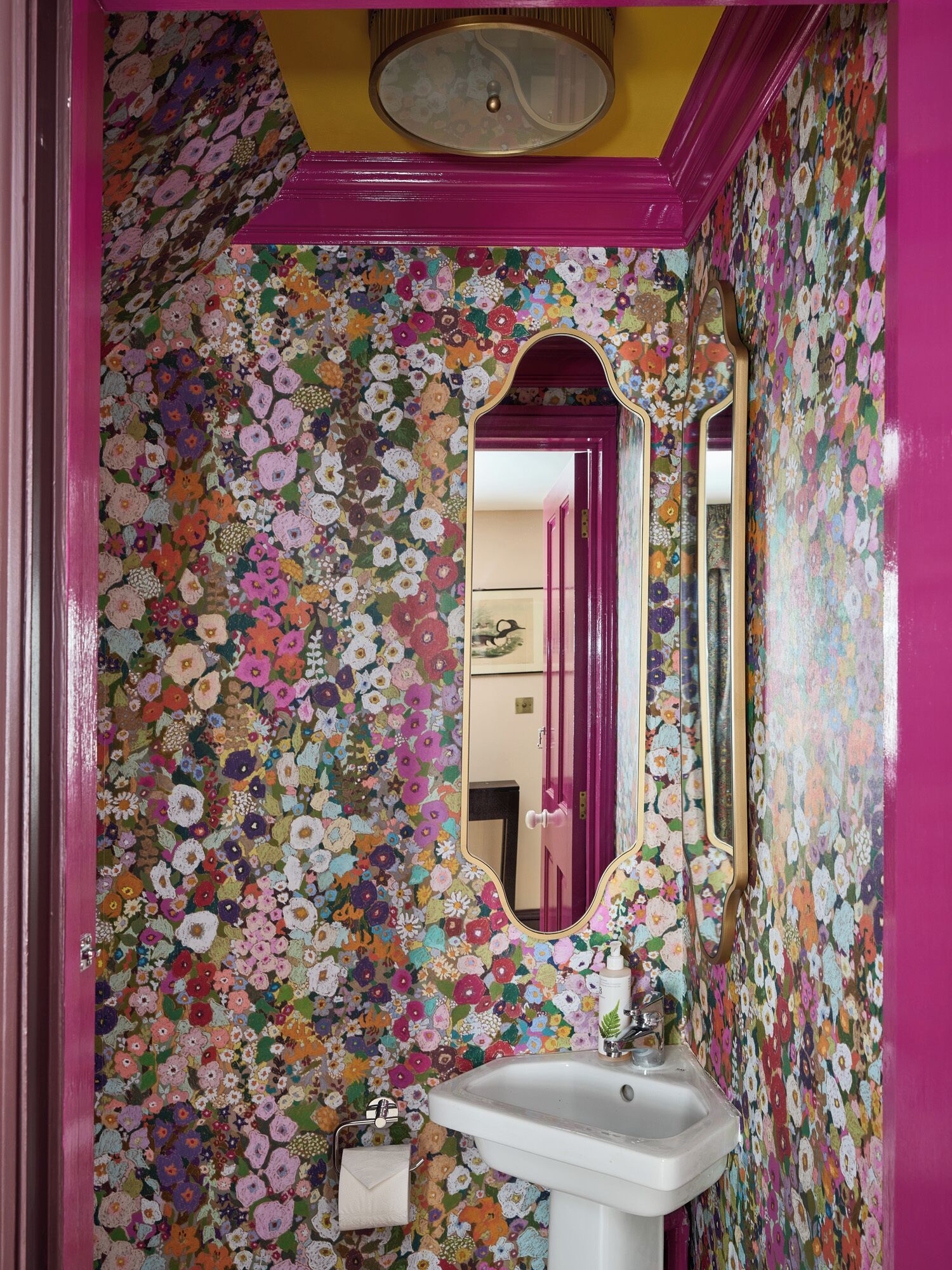 Un baño con papel tapiz floral, un tocador rosa y un espejo.