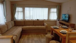 A cozy living room with a sofa, a dining table set for two, and a television on a stand.