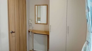 A room with a wooden door, a white radiator, a small shelf with a telephone, and a mirror on the wall.