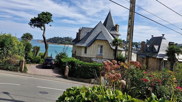 Une maison située sur la côte, avec un toit à forte pente, une cheminée en pierre et une vue sur la mer.