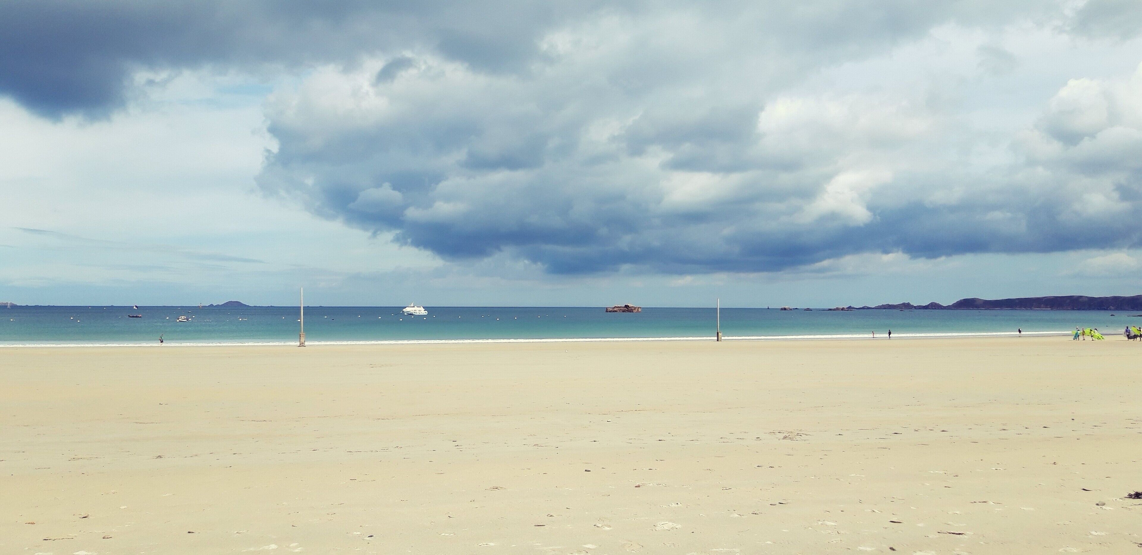 A beach with a wide sandy shore, a clear sky, and a few boats in the distance.