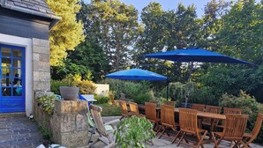 Une terrasse extérieure avec des meubles en bois, un parasol bleu et un mur en pierre.
