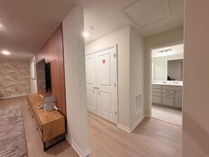 A modern apartment with a wooden entertainment unit, a double door closet, and a bathroom with a large mirror and vanity.