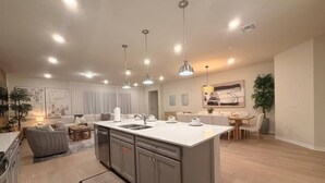 A modern kitchen with a central island, pendant lighting, and a dining area with a table and chairs. - Luxury Oasis 8BR Villa - Windsor Cay Resort (Clermont)