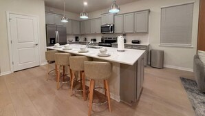 A modern kitchen with a central island, bar stools, stainless steel appliances, and pendant lighting. - Luxury Oasis 8BR Villa - Windsor Cay Resort (Clermont)