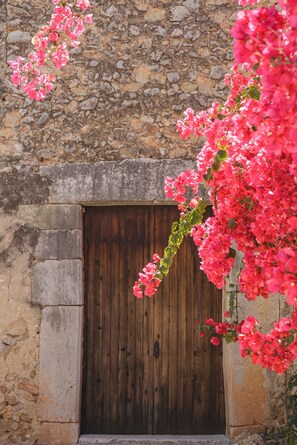 A stone building with a wooden door and pink flowers in front.