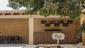 A bar area with wooden tables and benches, a stone wall, and a sign reading "Bar". - Finca Binissatí by Mallorca North Villas (Inca)
