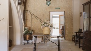 A hallway with a rustic wooden ceiling, a woven basket with flowers, a metal lamp, and a door labeled "SALIDA DE BARRIO". - Finca Binissatí by Mallorca North Villas (Inca)