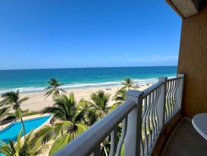 Ein Balkon mit Blick auf einen Strand, Palmen und ein Schwimmbecken.