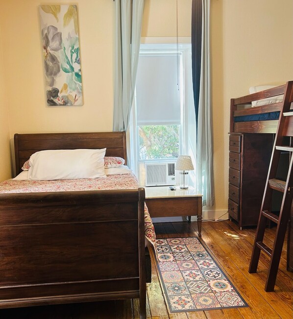 A bedroom with a bed, a dresser, a chair, a window with curtains, and a radiator. - Hill Country Guest House (Mason)
