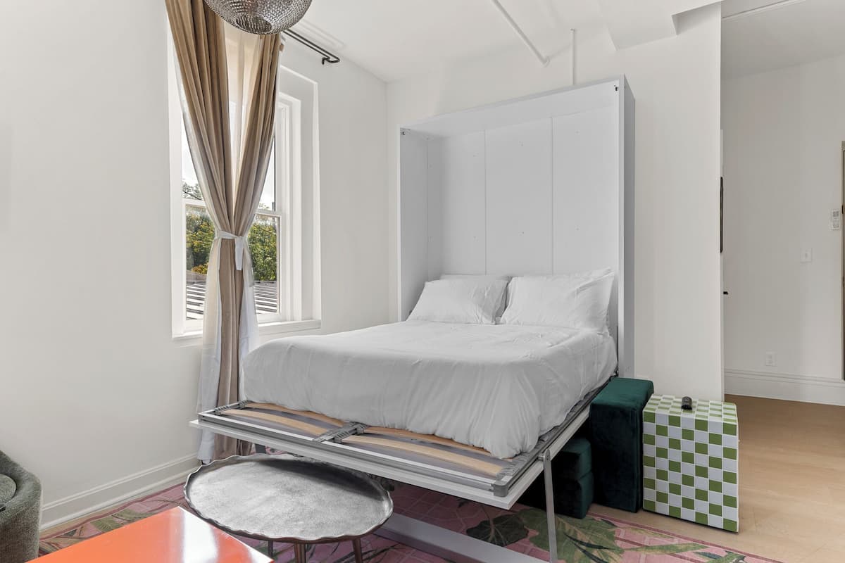 Ein schlicht eingerichtetes Schlafzimmer mit einem Bett, einem kleinen Tisch und einem karierten Hocker.